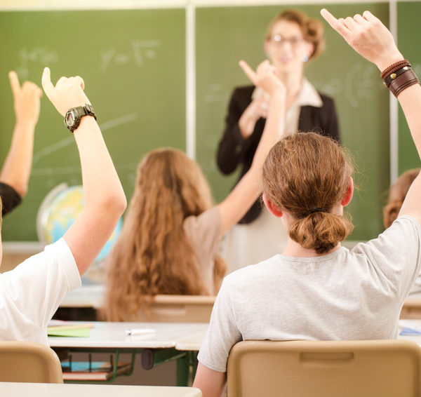 Teacher or docent standing while lesson in front of a blackboard or board and educate or teaching students or pupils or mates, which notify and learn in a school or class